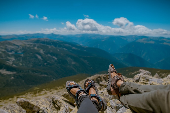 picture of two persons on a mountain sitting on the rocks, wearing pants and sandals