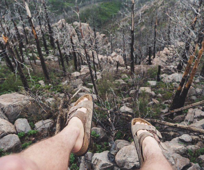 picture of person sitting on a cliff with a view of rocks and threes wearing brown cork slip-on sandals