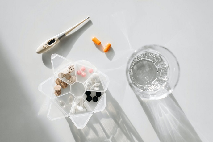 picture of box with different pills, thermometer and a glass of water on a white table