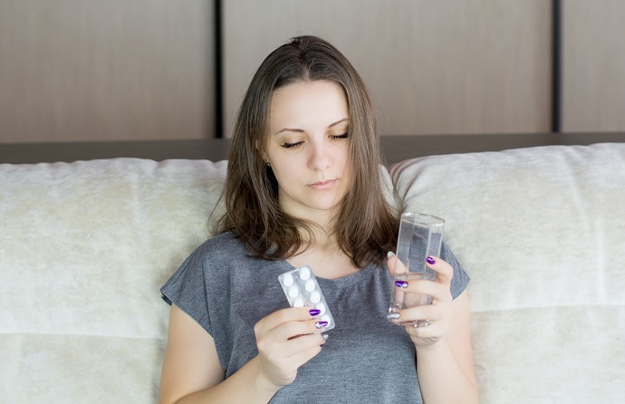 picture of a woman in bed holding pills and a glass of water 