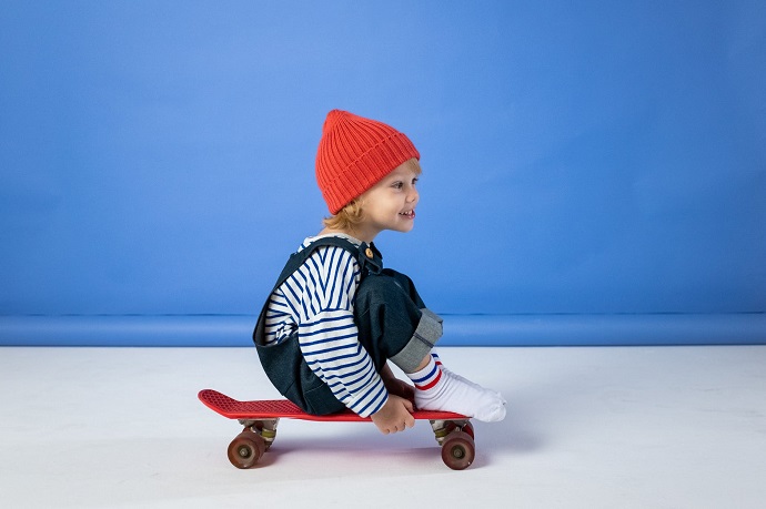 picture of a kid in front a blue wall sitting on a skateboard 